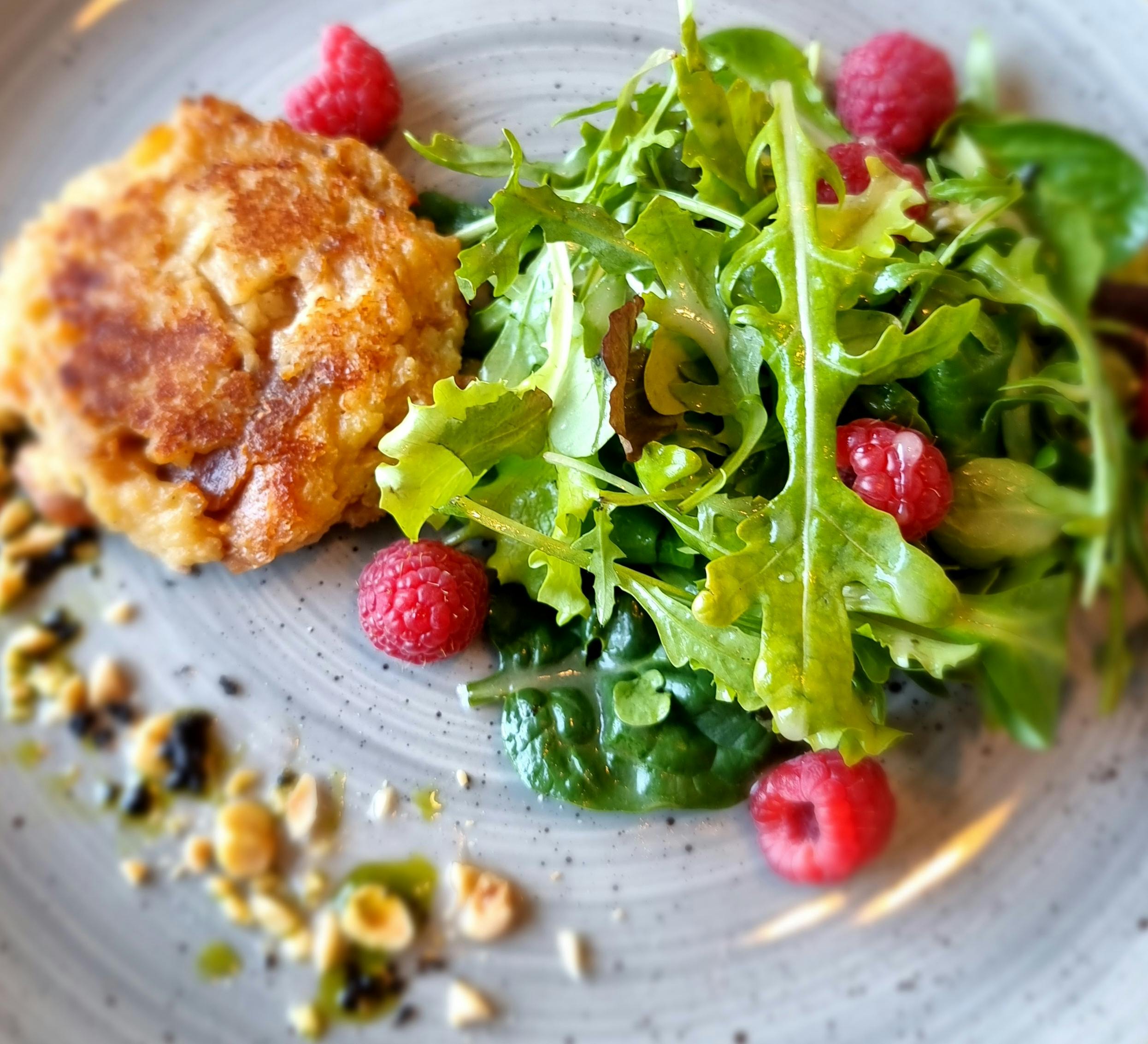 Close-up of a gourmet meal featuring a salmon cake, fresh arugula salad, and raspberries.