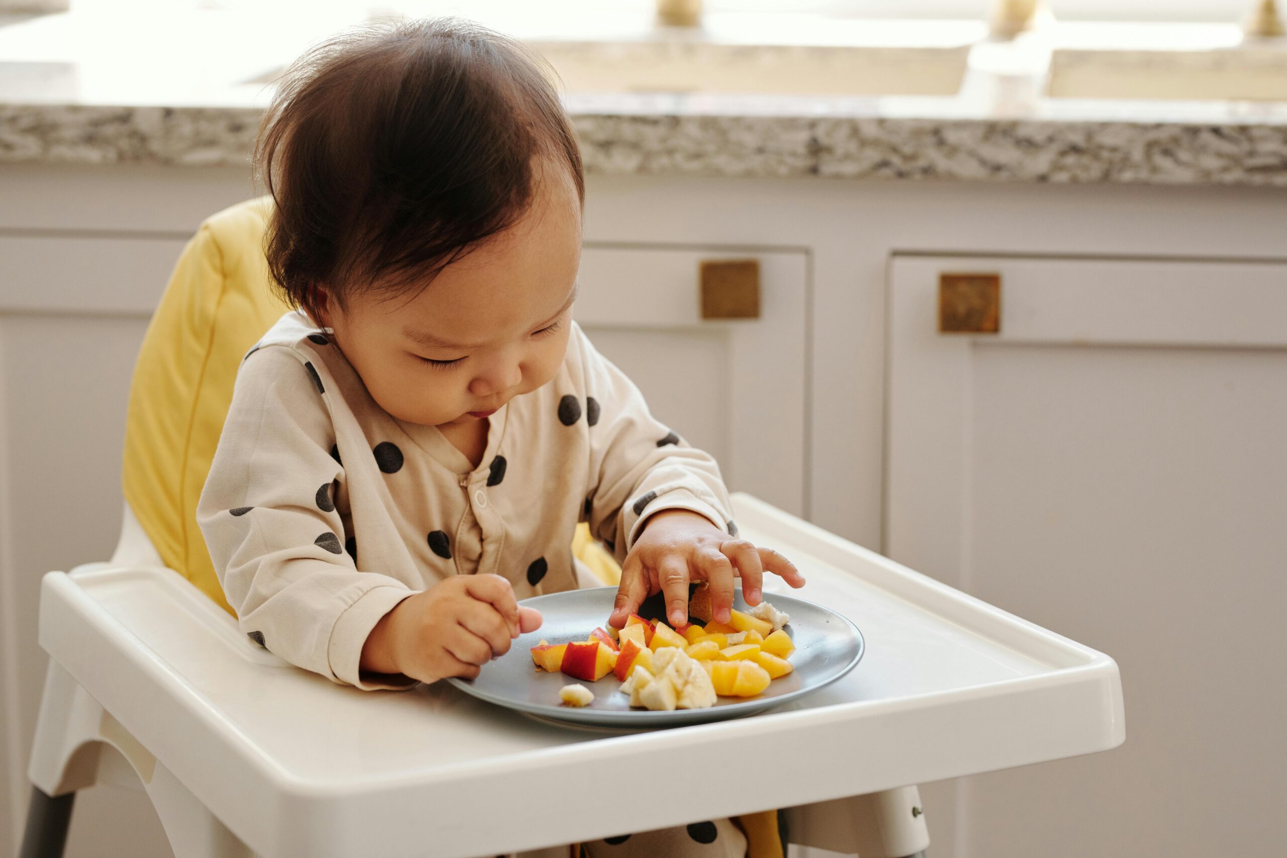 A cute toddler in a polka dot outfit enjoying a healthy fruit snack indoors.